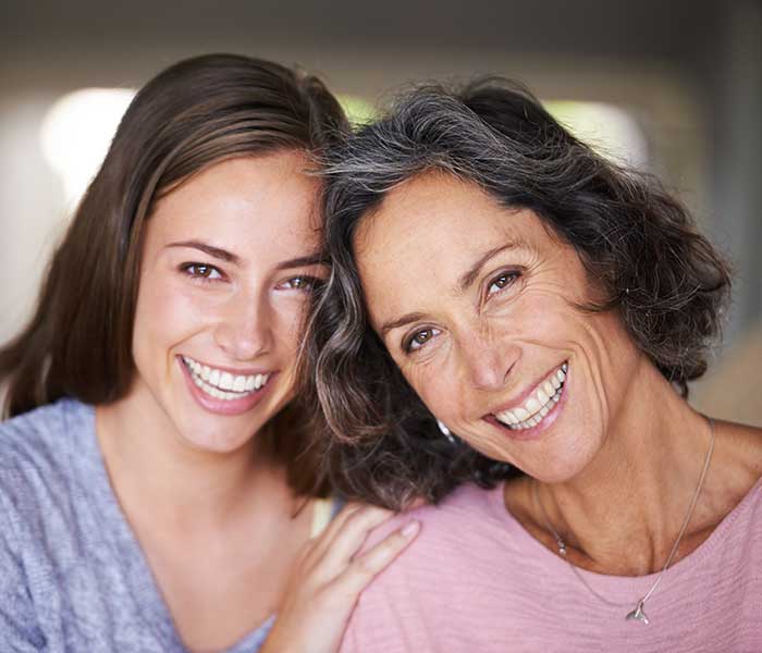 A laughing mother and daughter standing in their home and looking at the camera