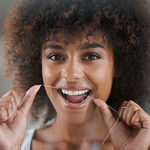 young woman flossing her teeth in the mirror